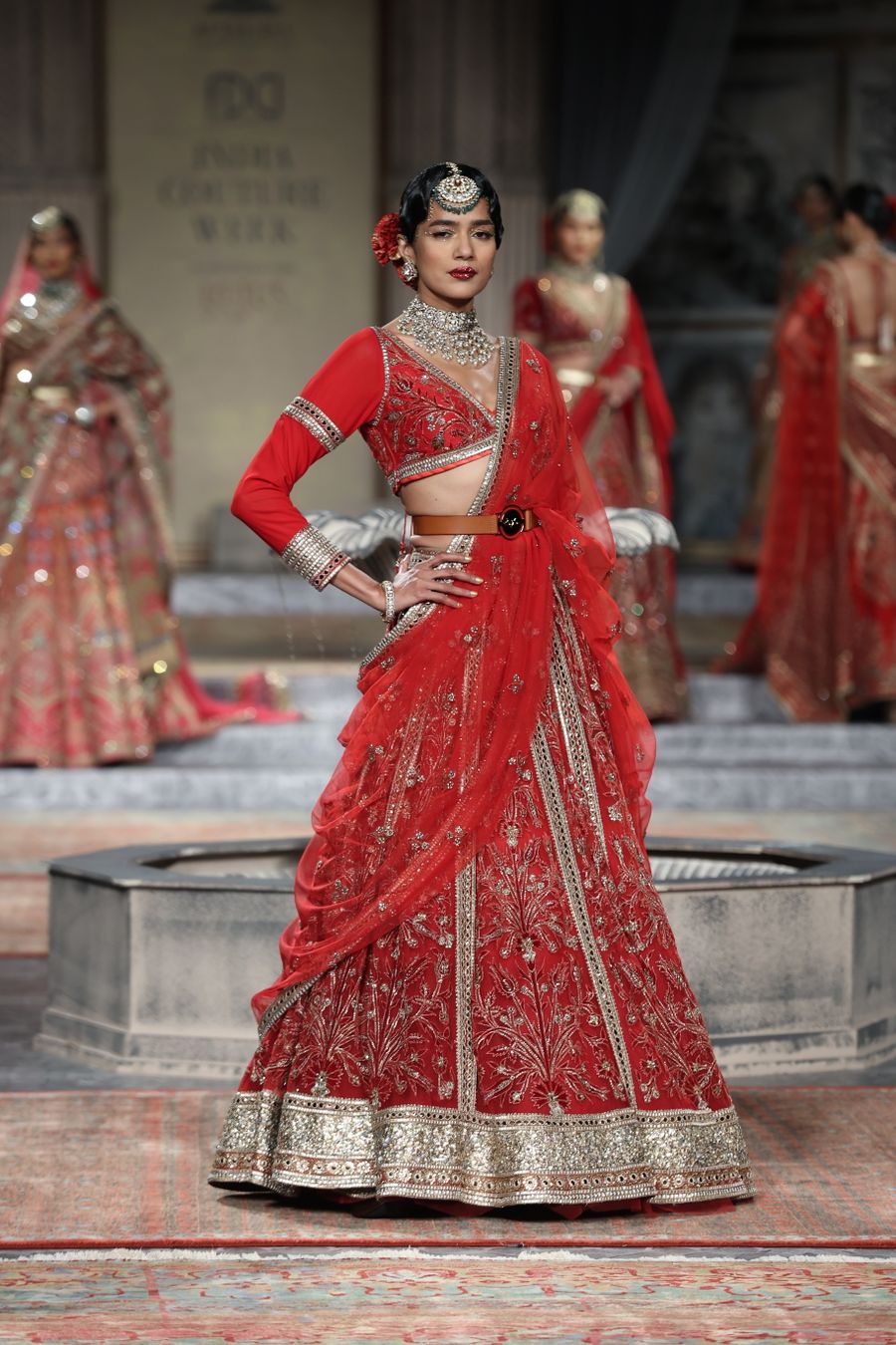 Model on a couture runway in a red hand-embroidered bridal lehenga