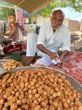 An elderly man selling traditional sesame sweets at an outdoor market, showcasing cultural trade.