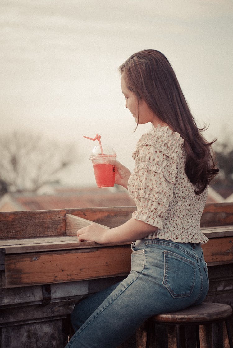 A Woman Sitting At A Brown Wooden Counter Holding Pink Beverage