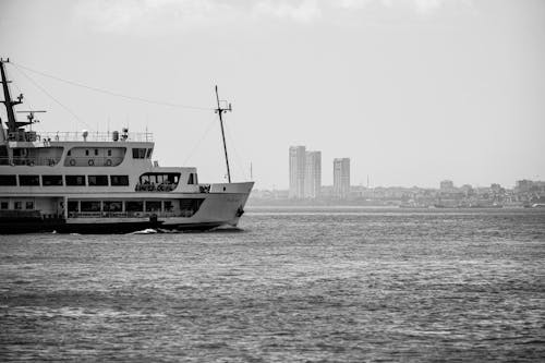 Grayscale Photo of a Ship on Sea Near City Buildings