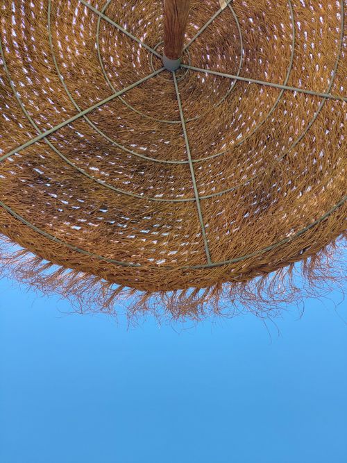 Free Close-up view of a straw umbrella resembling a sun hat against a blue sky. Stock Photo