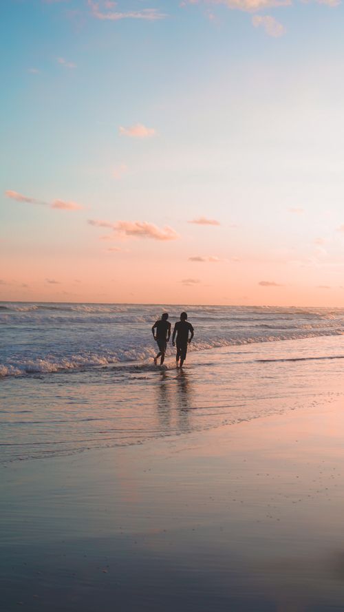 Free Two people walking on a tranquil beach during a beautiful sunset with soft pastel hues in the sky. Stock Photo