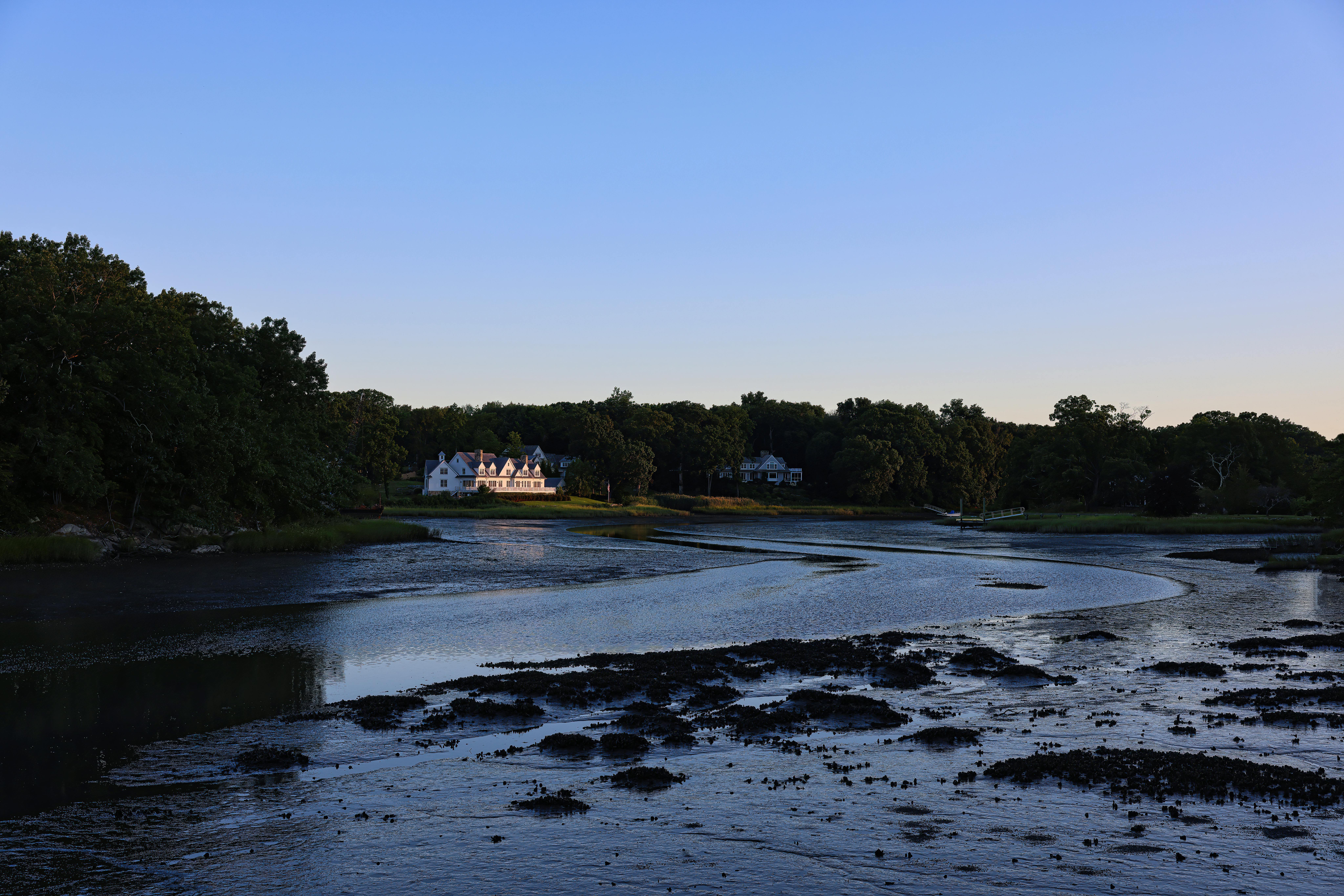 Peaceful lakeside scene in Darien, CT, with a distant house at sunrise.