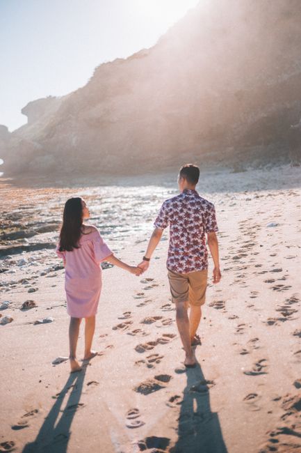 Young couple strolling hand in hand on a sunny beach, leaving footprints in the sand.
