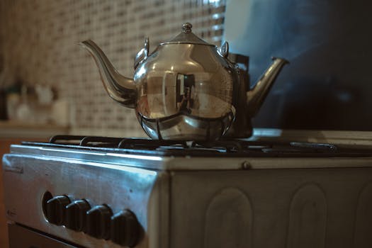 A reflective stainless steel kettle sits on a kitchen stove, capturing a warm indoor ambiance.