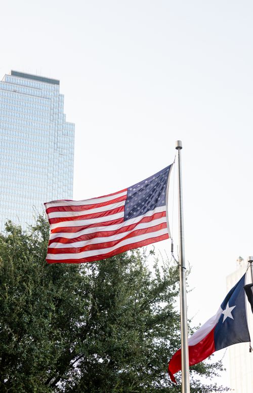 Free A dynamic view of the American and Texas flags waving against a modern skyscraper backdrop. Stock Photo