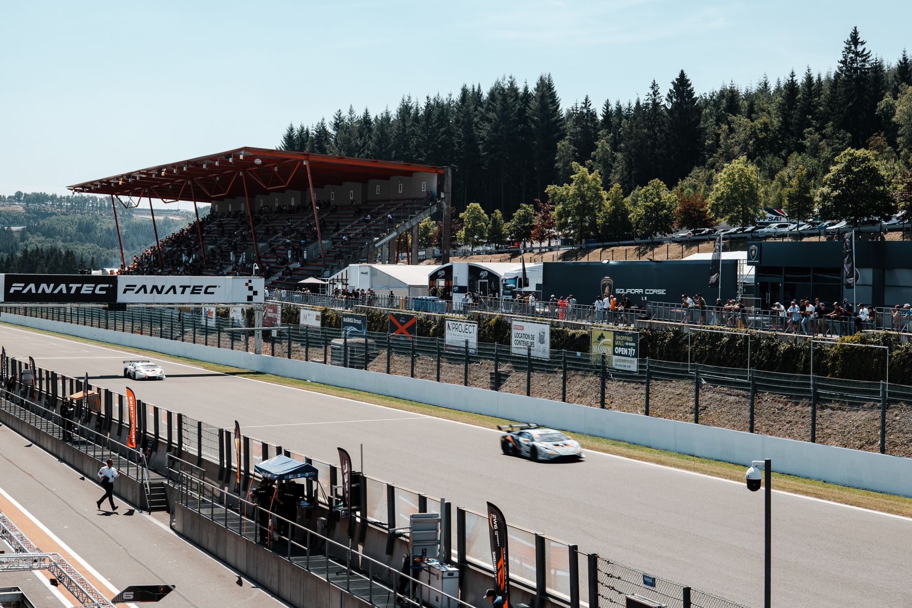 Racecars speeding on a track with spectators, showcasing high-speed motorsport action.