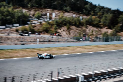 Free Blurred motion of a fast sports car on a sunny race track circuit surrounded by trees. Stock Photo