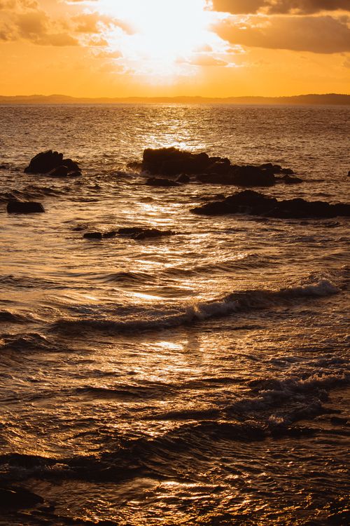 Free Captivating view of the sun setting over the ocean, with waves crashing on rocks. Stock Photo