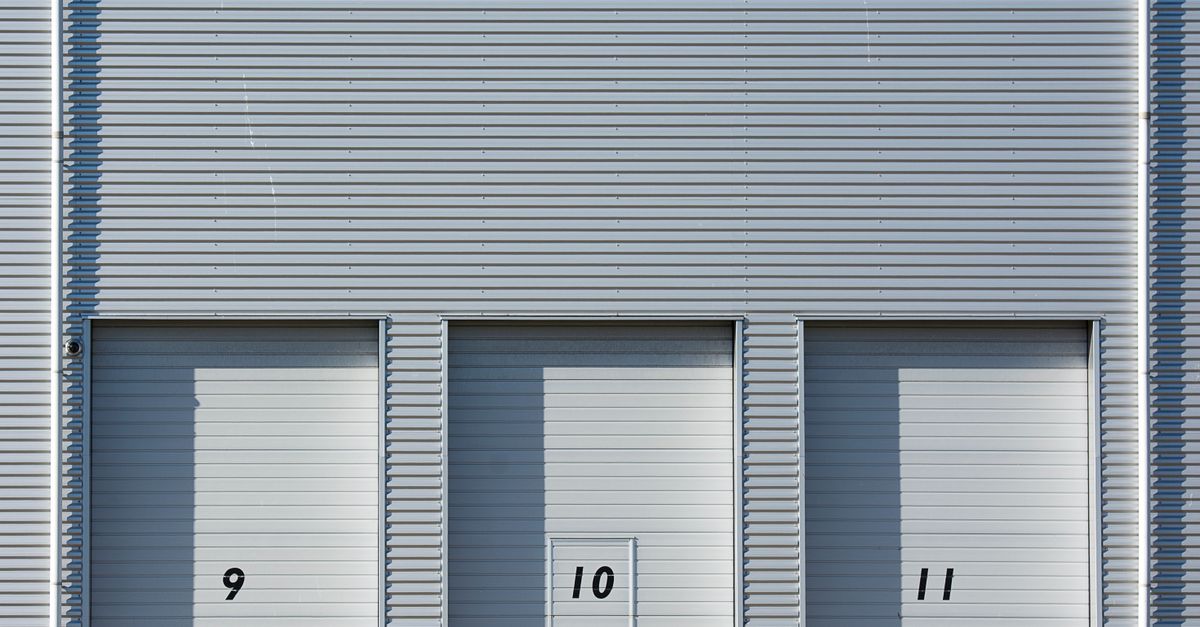Close-up view of a modern industrial building with metal shutters numbered 9, 10, and 11, showcasing minimalist architecture.