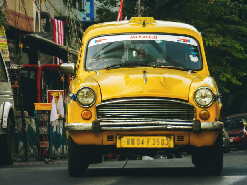 Classic yellow taxi driving through the vibrant streets of Kolkata, India.
