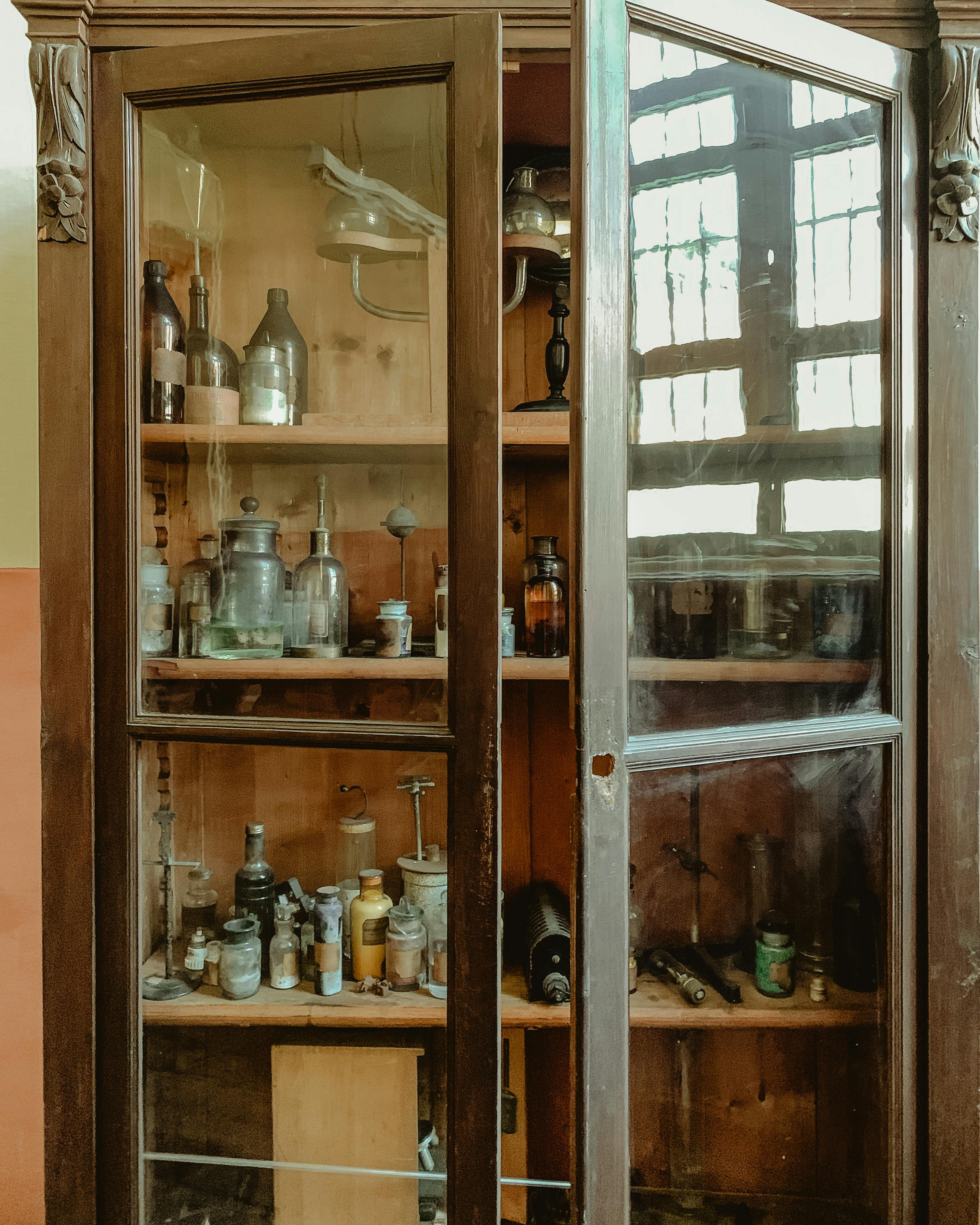 Explore a wooden vintage cabinet filled with various antique bottles on glass shelves.