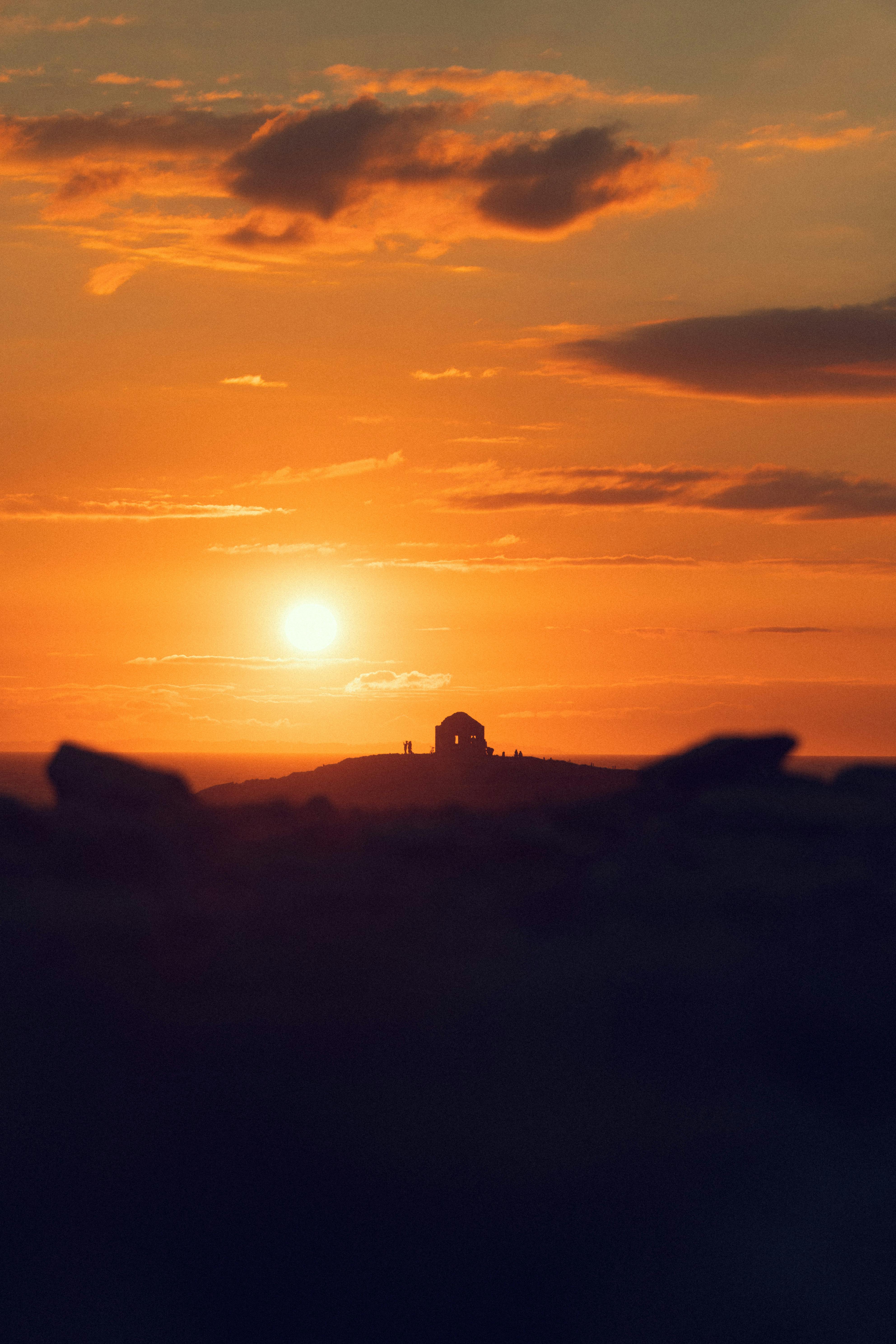 A serene silhouette of a house on a hill against a vibrant sunset sky.