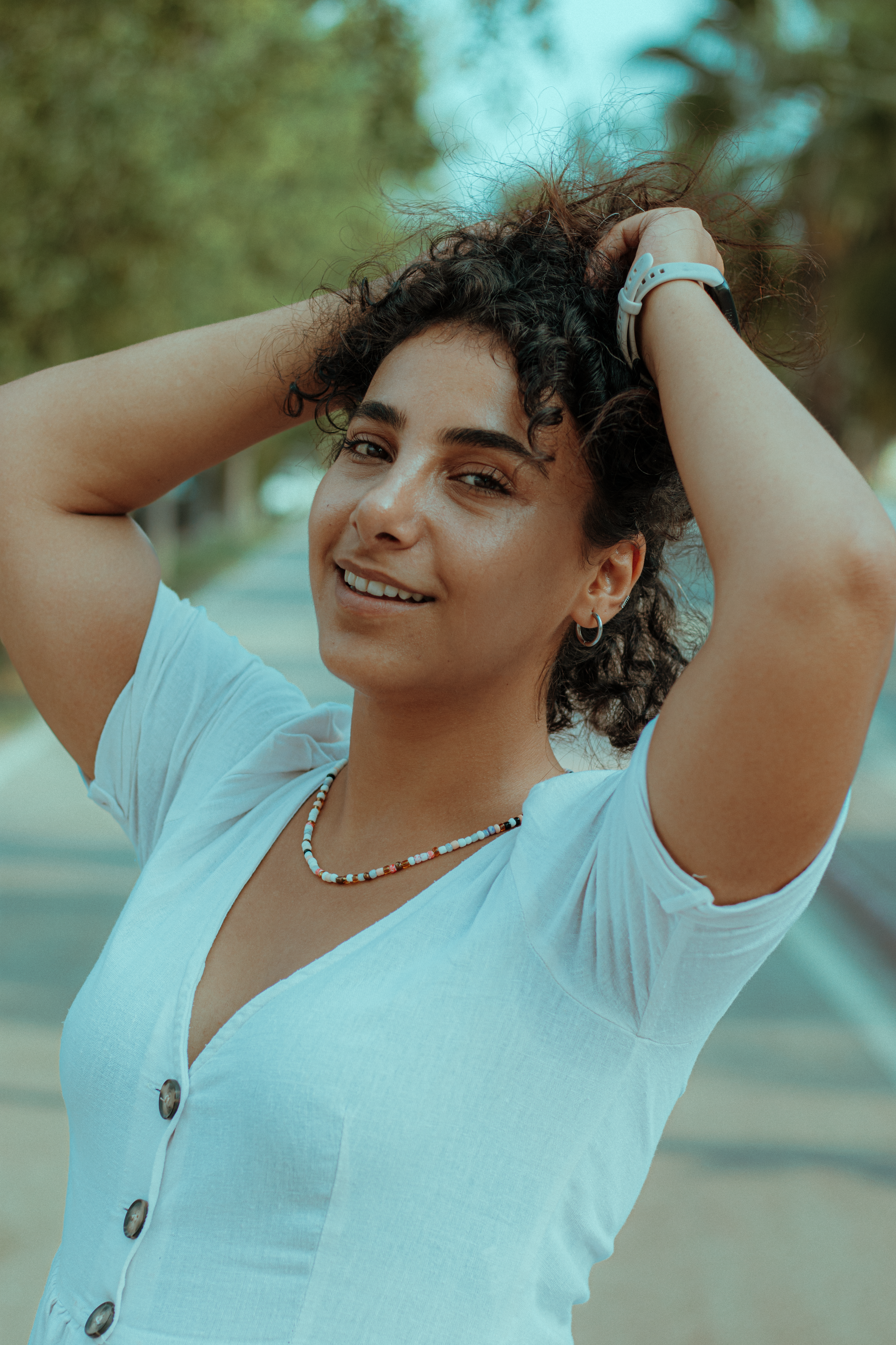 A cheerful woman with curly hair smiling under the sun, showcasing natural beauty and joy.