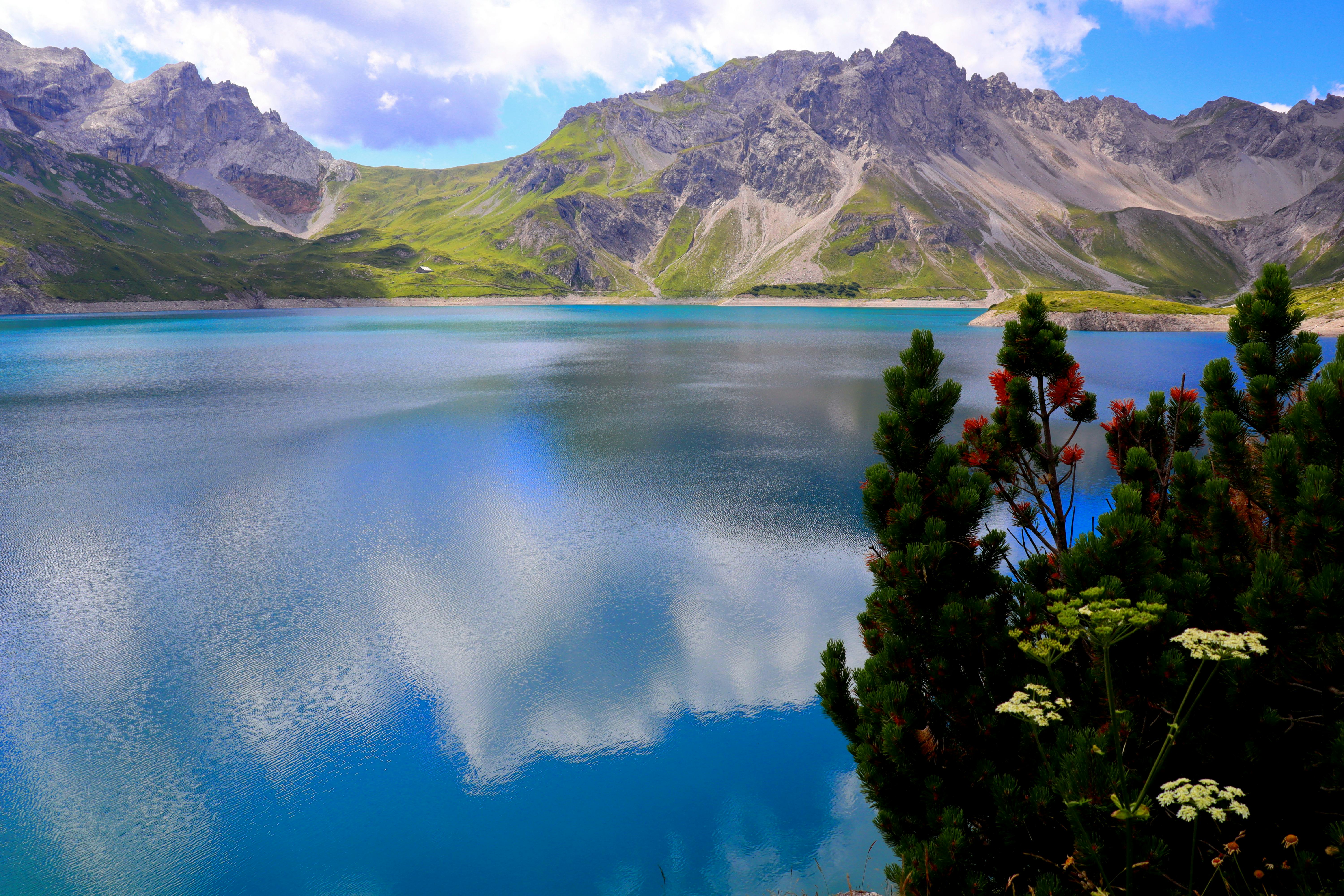 A serene mountain lake reflecting surrounding peaks and clouds in a peaceful natural setting.