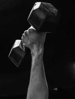 Black and white photo of a hand holding up a heavy dumbbell, focusing on strength and fitness.