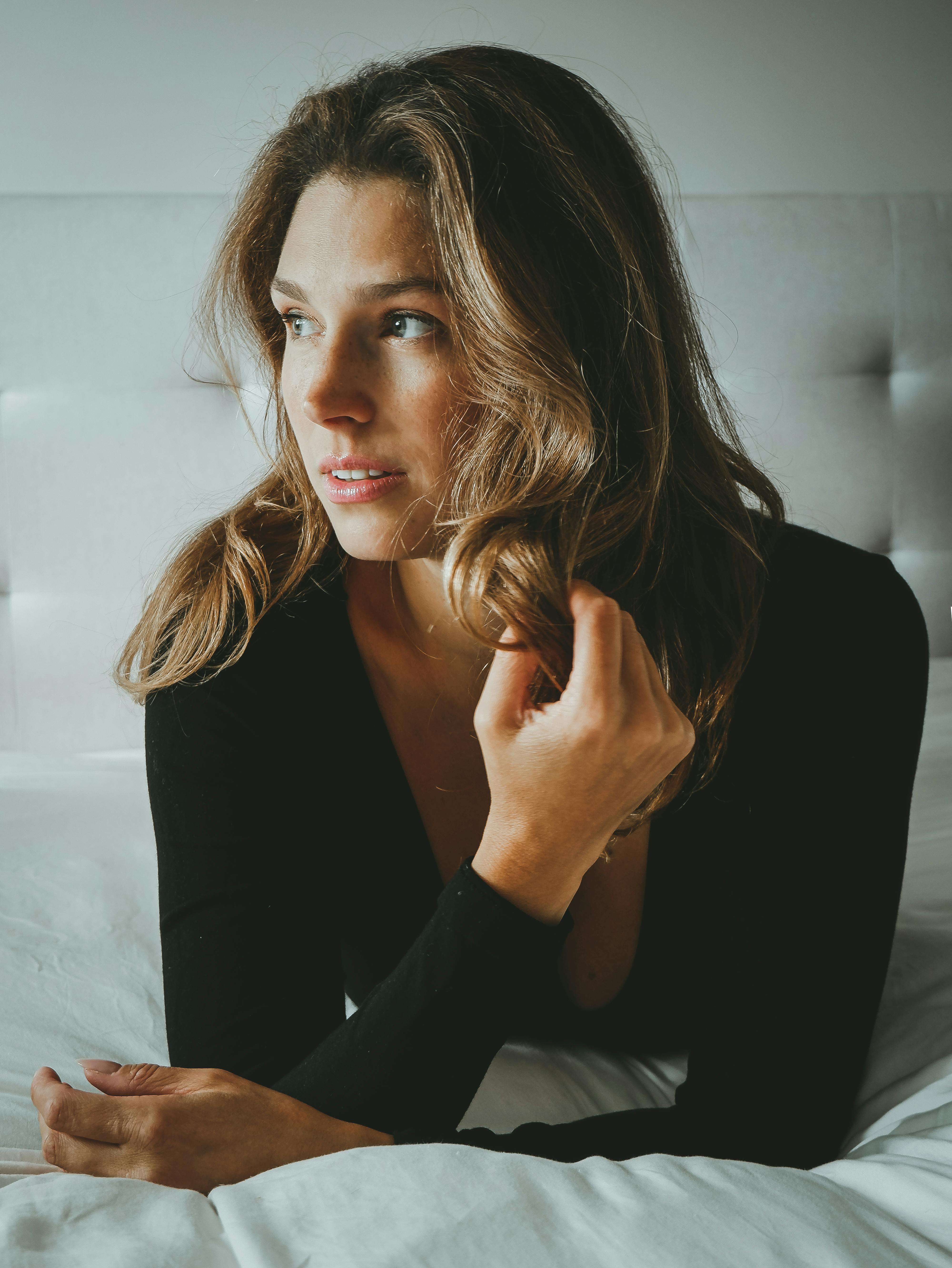 A thoughtful woman lying on a bed with soft lighting and relaxed ambiance.