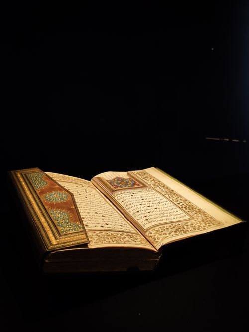 Free Ancient Quran open with intricate Arabic calligraphy, illuminated against a dark background, showcasing religious artistry. Stock Photo