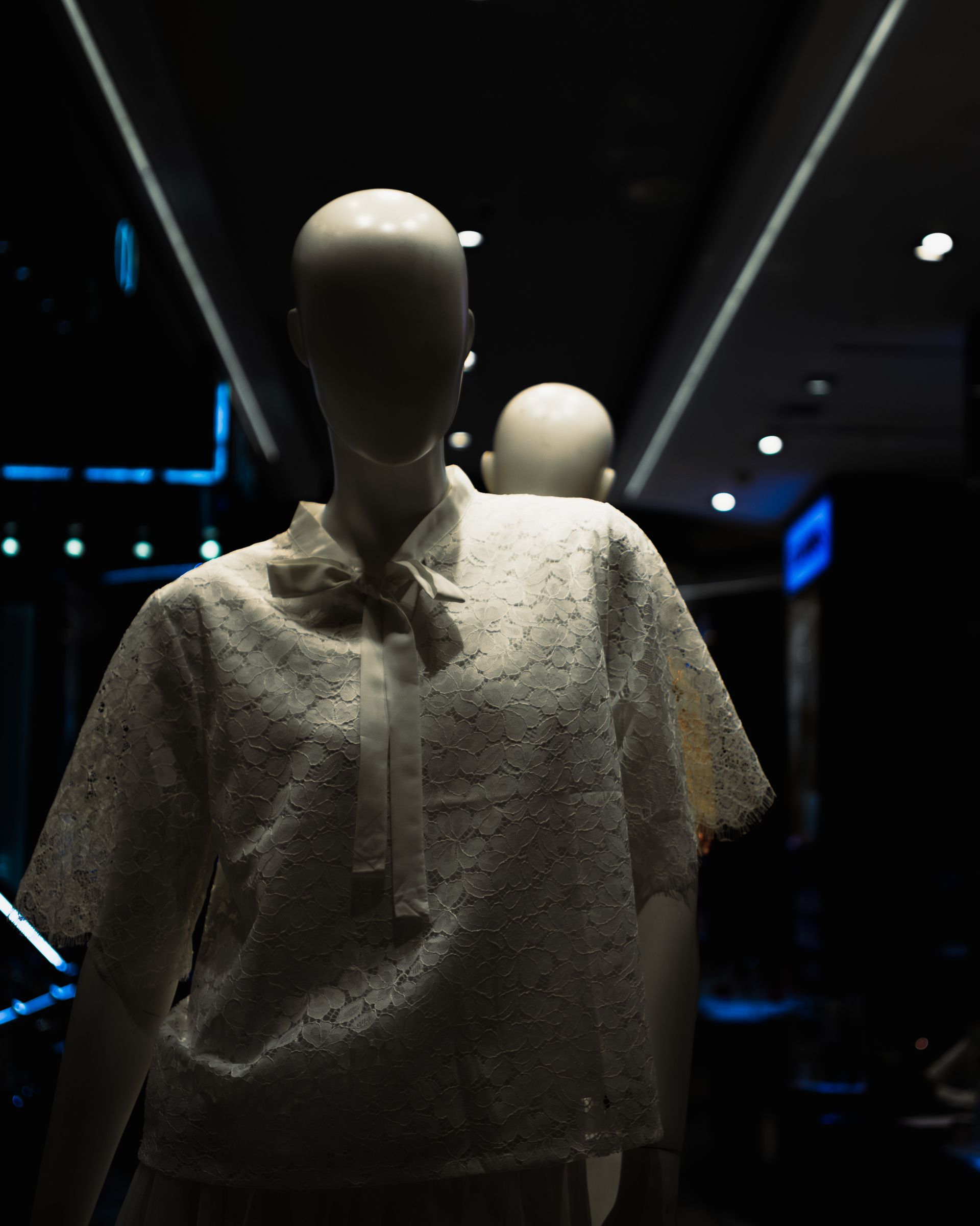A mannequin wearing lace clothing, set in a dark, modern fashion store interior