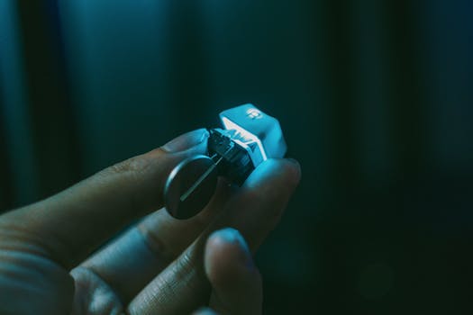 A close-up view of a hand holding a mechanical keyboard switch with a keycap attached.