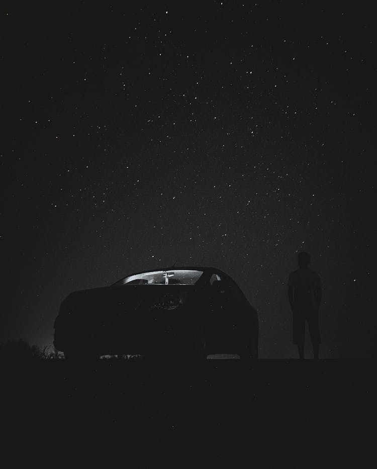 Silhouette Of A Person Standing Beside Car Under A Starry Sky