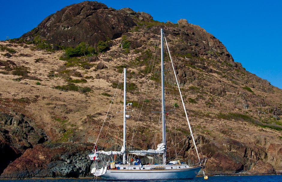 Best Waikiki Private Day Tour and Sunset Sail for Couples Review: The Ultimate Romantic Oahu Experience Review 2026 - A sailboat anchored by a rocky mountain coastline under clear blue skies, ideal for travel and adventure settings.