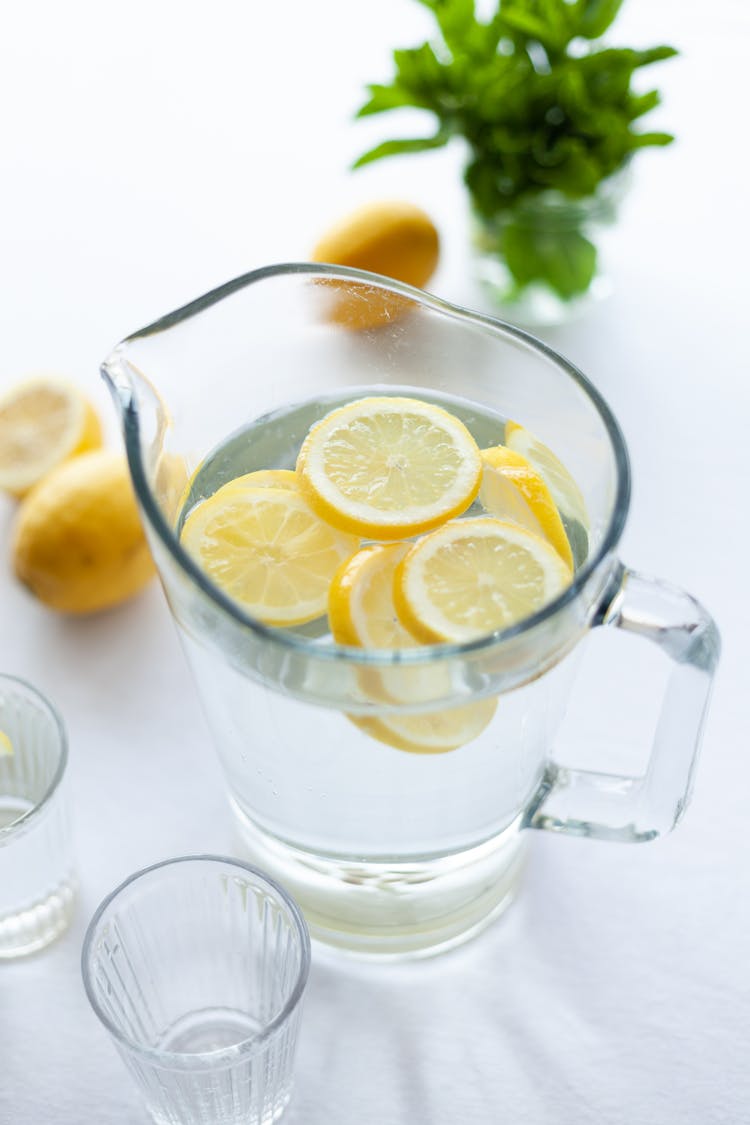 Clear Glass Pitcher Filled With Clear Liquid And Slices Of Lemon