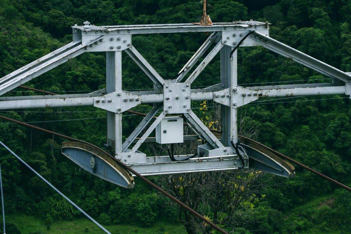 Detailed metalwork of Mérida cable car system amidst lush greenery.