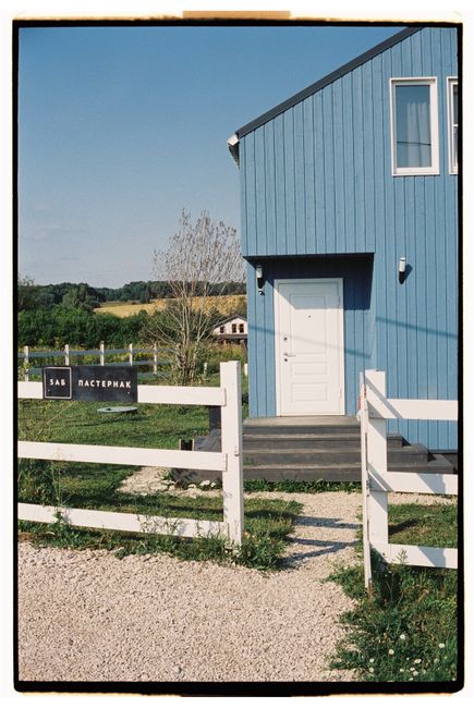 Blue wooden house in Dvoryaninovo, Tula Oblast, Russia with white fence and lush greenery.