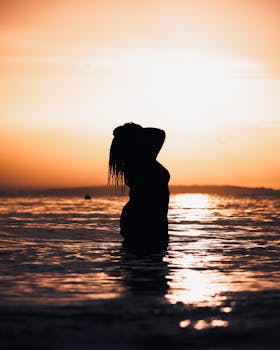 A serene silhouette of a woman in the ocean during a vibrant sunset, capturing tranquility and beauty.