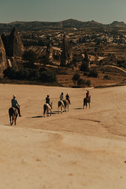 Free Riders on horseback explore the unique rock formations of Cappadocia, Turkey under a sunny sky. Stock Photo