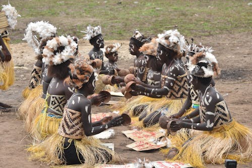 People Wearing Tribal Clothing and Feather Plumes Sitting on a Ground with Coconut Shells