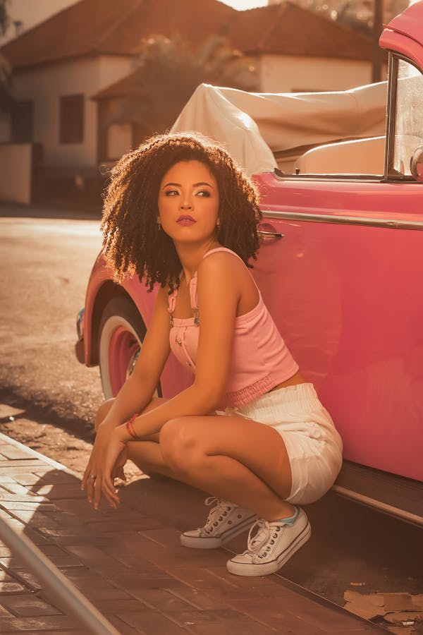 Woman in White Tank Top and White Shorts Sitting on Red Car