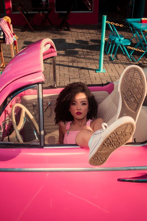 Free A fashionable woman sits in a pink vintage car on a sunny day, exuding casual elegance. Stock Photo