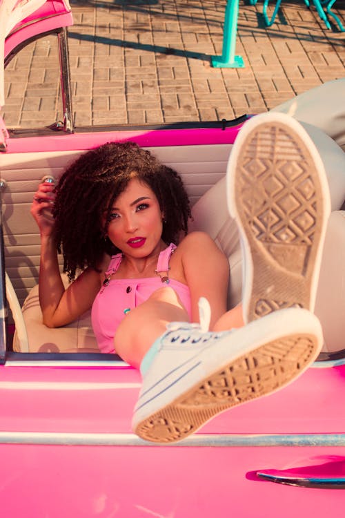Free Woman Posing in a Pink Cabriolet and Showing Shoe Soles to the Camera Stock Photo