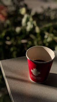 A red disposable cup with a maple leaf design casting a shadow on a table.
