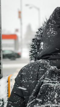 A person wearing a coat with snow falling heavily during a winter day.