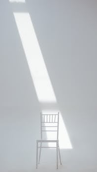 A white chair in a minimalistic setting with sunlight casting a dramatic shadow.