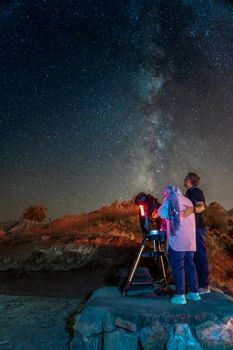 Couple observing the Milky Way in Iran using a telescope. Starry night sky.