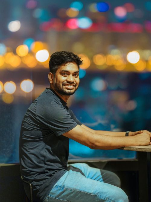 Free A cheerful man in casual attire smiles with colorful bokeh lights in the background. Stock Photo