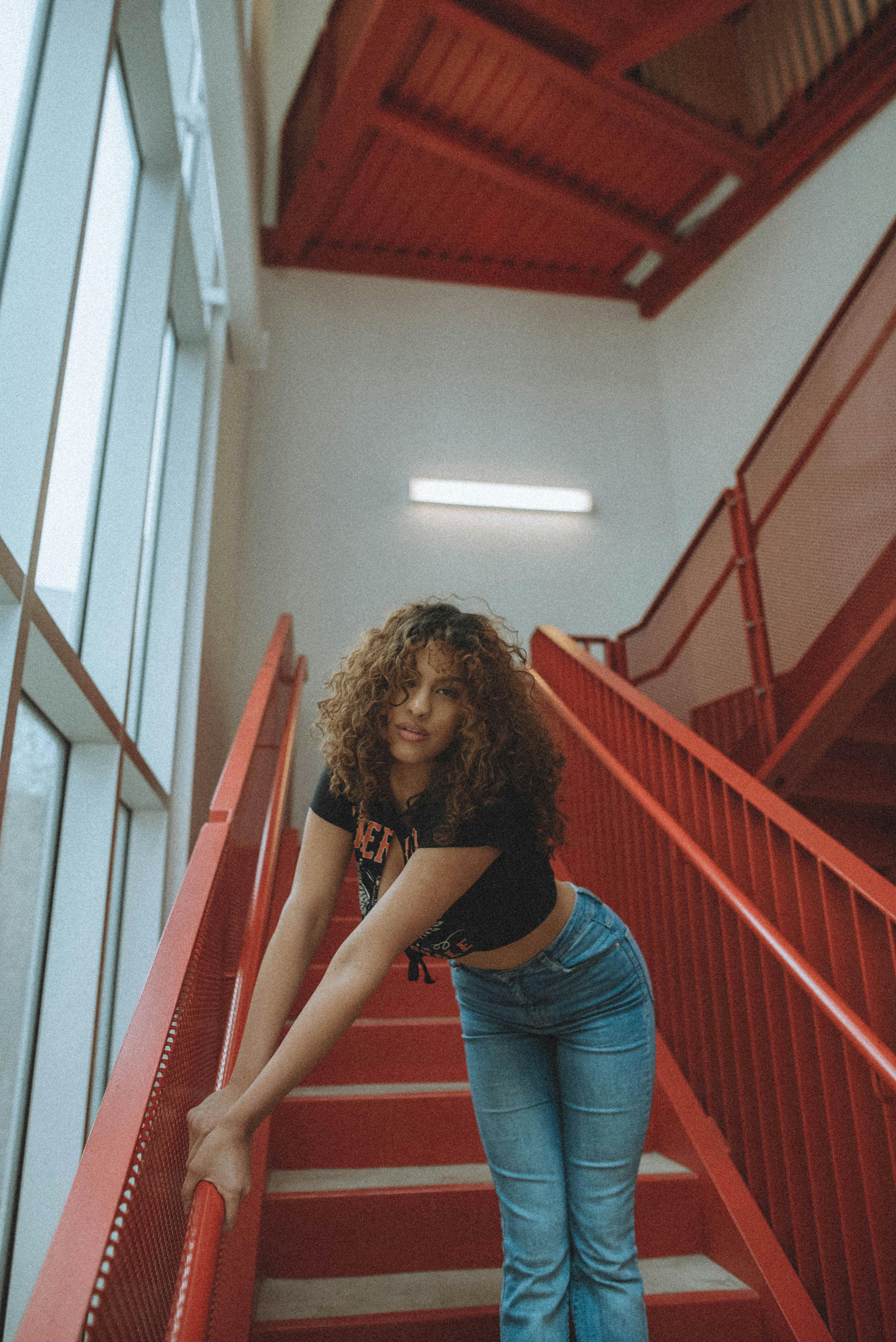 Brunette woman in denim and crop top posing on red staircase indoors.