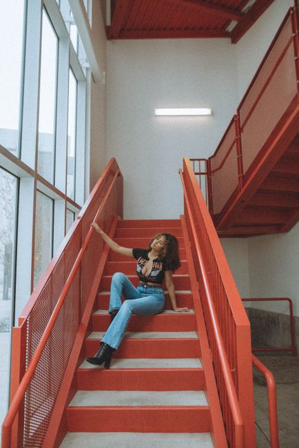 Stylish young woman poses on a striking red staircase in an indoor setting.