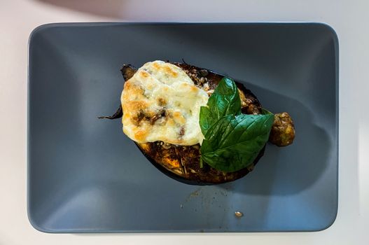 Appetizing baked eggplant topped with mozzarella cheese and fresh basil leaves on a plate.