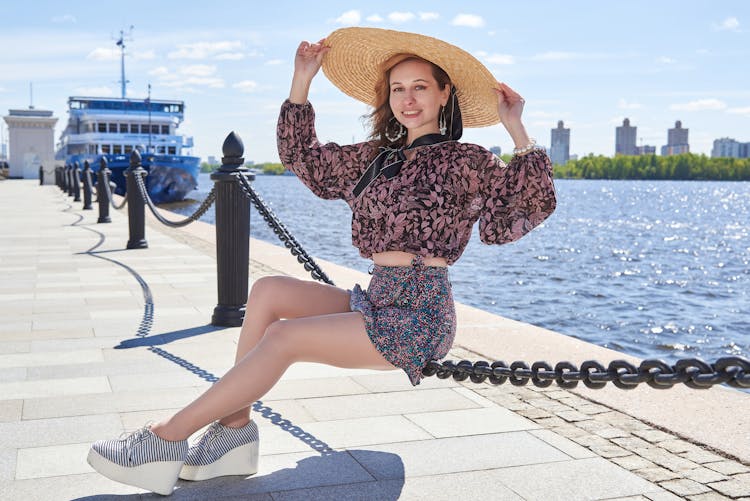 Woman In A Summer Outfit Sitting On A Pier In City 