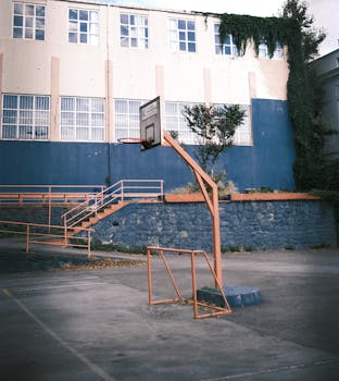 Rustic outdoor basketball court with a hoop and aged school building in urban setting.