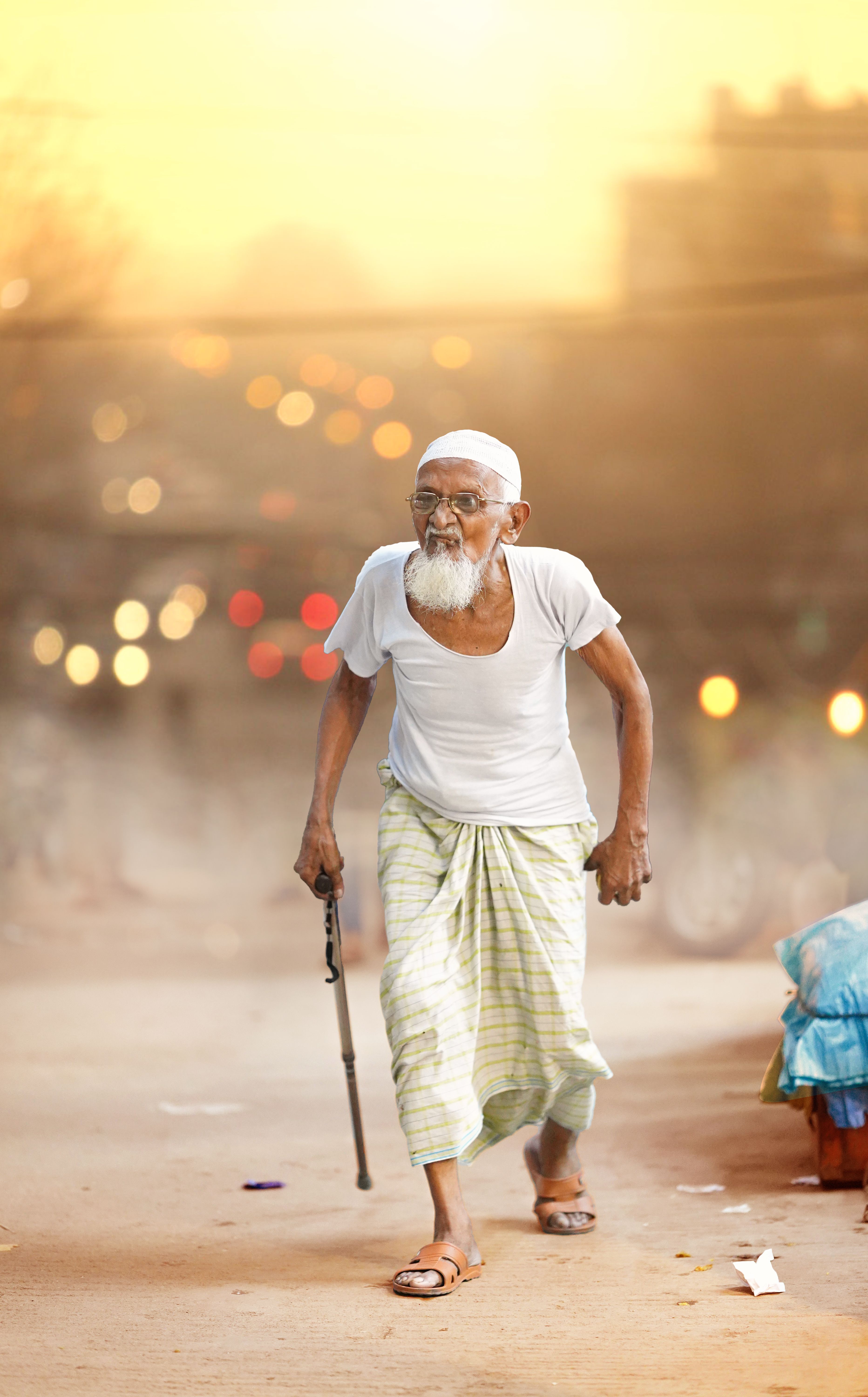 Senior man with a walking stick strolling on a street at sunset, showcasing determination and resilience.
