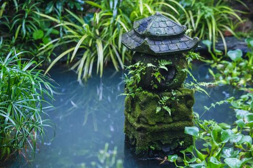 Free A tranquil stone lantern covered in moss within a lush garden pond setting, surrounded by greenery. Stock Photo