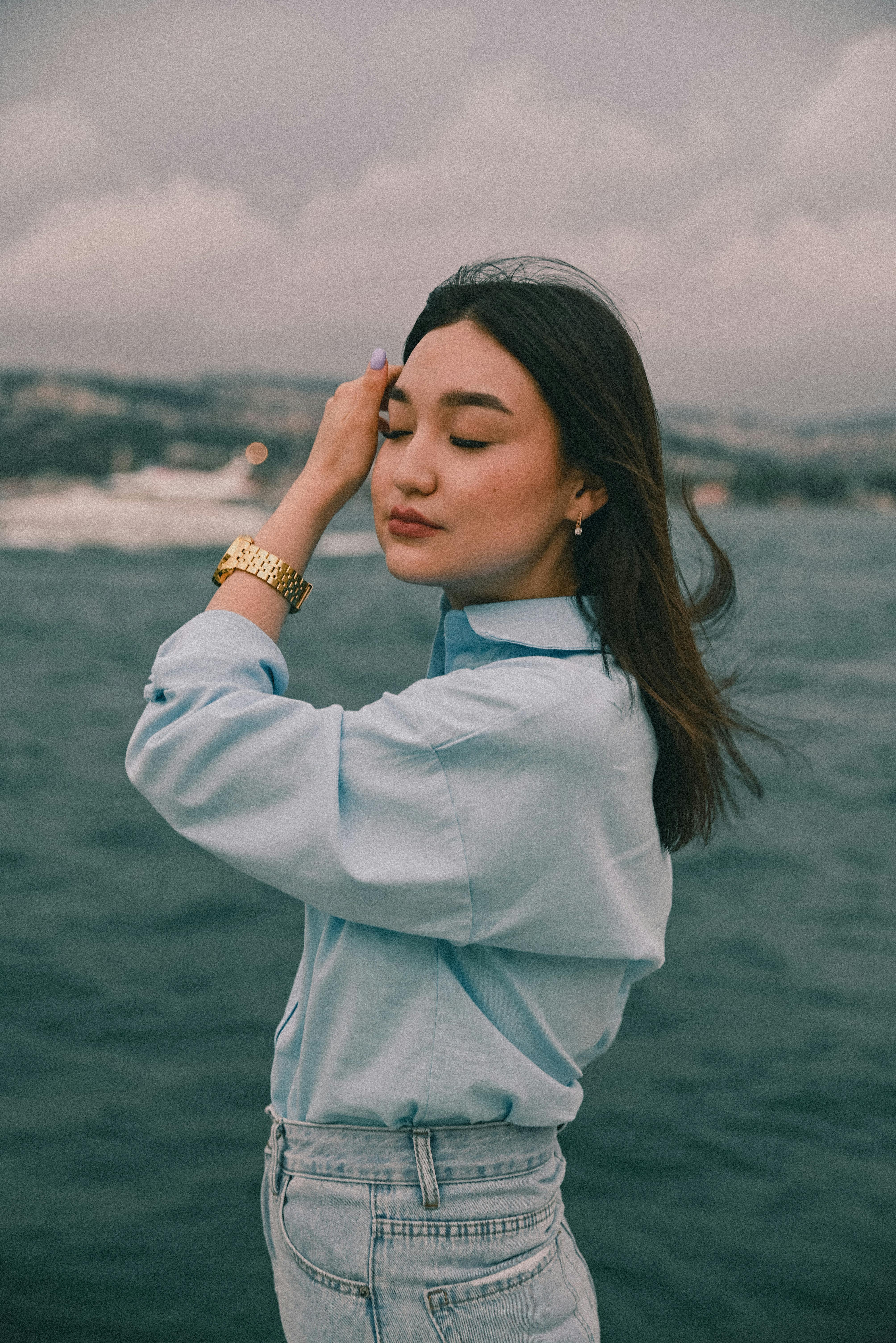 A woman standing by the ocean with eyes closed, feeling the wind.