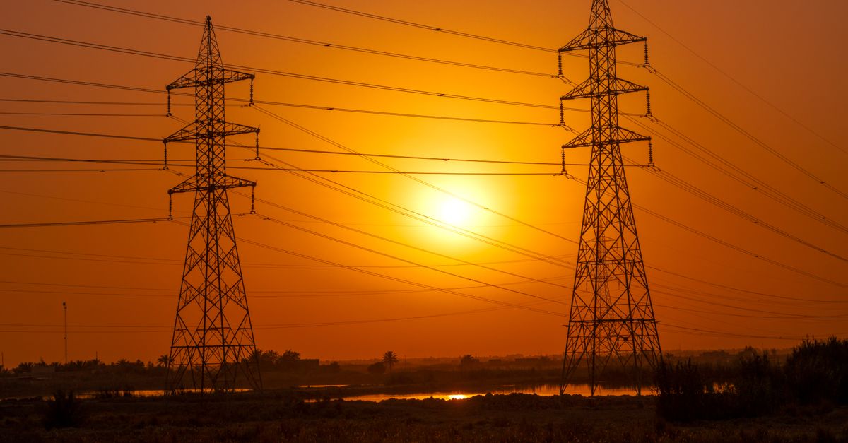 Silhouetted transmission towers under a vibrant sunset in Baghdad, Iraq.