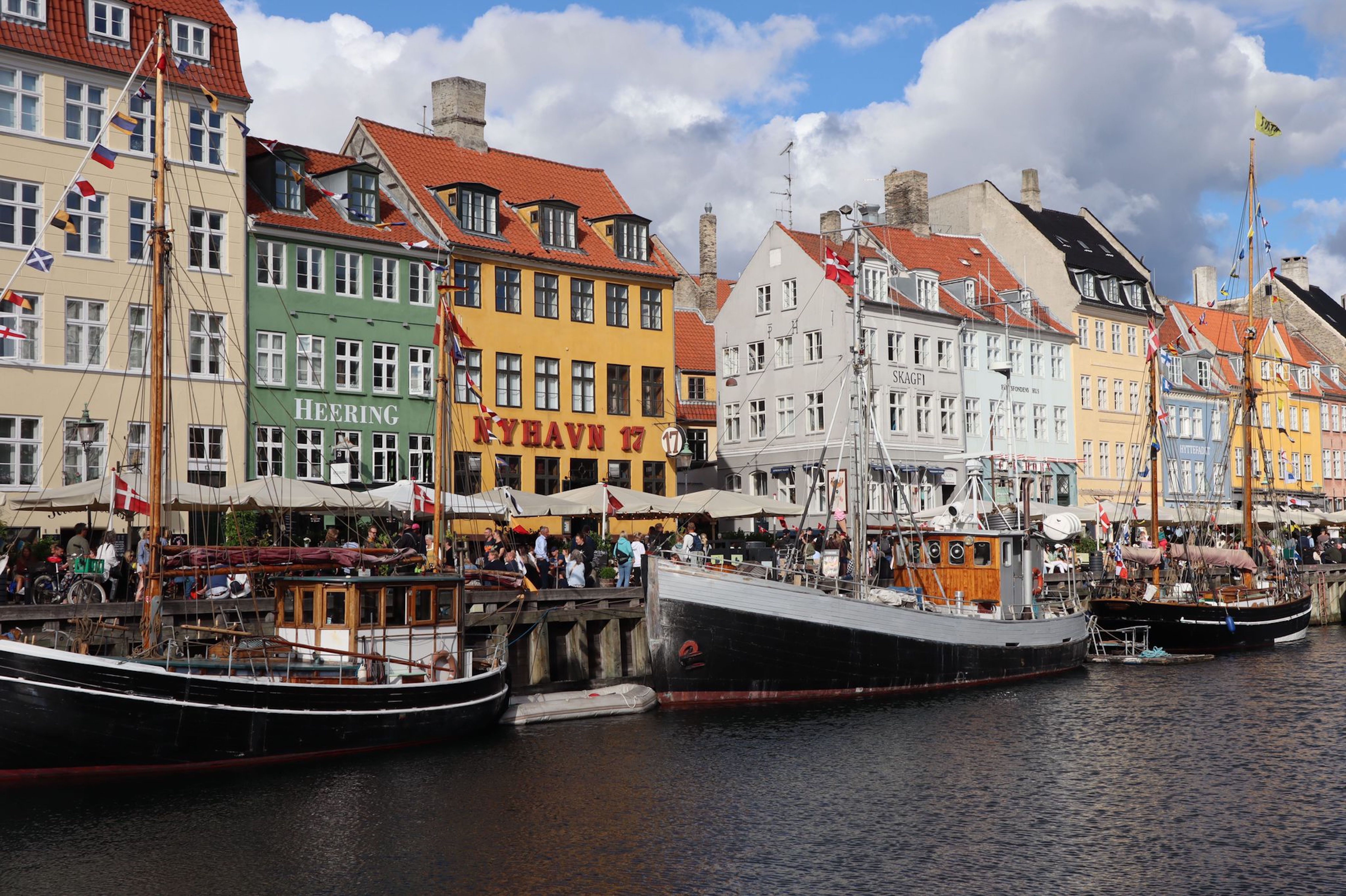 Scenic view of Nyhavn in Copenhagen with colorful buildings and moored wooden boats showcasing Danish culture.